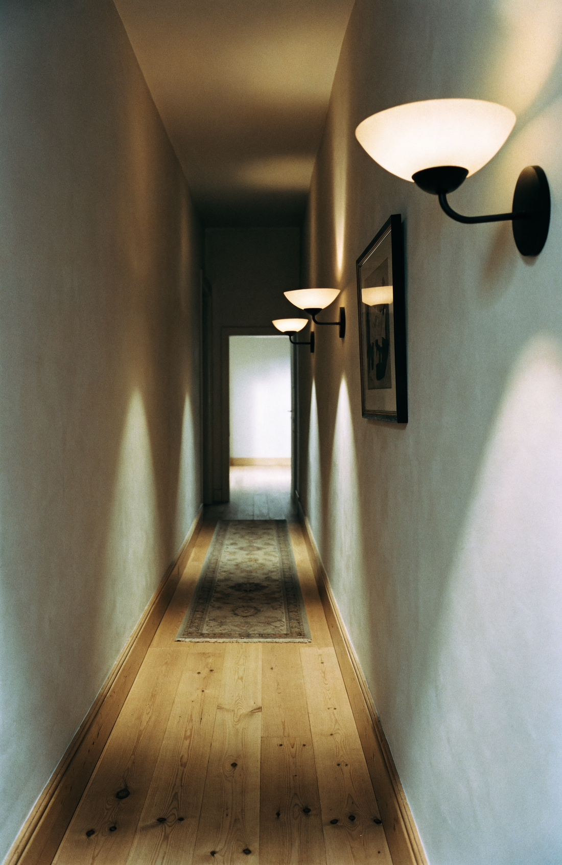 Three matte black wall sconces spaced evenly along a plaster hallway wall