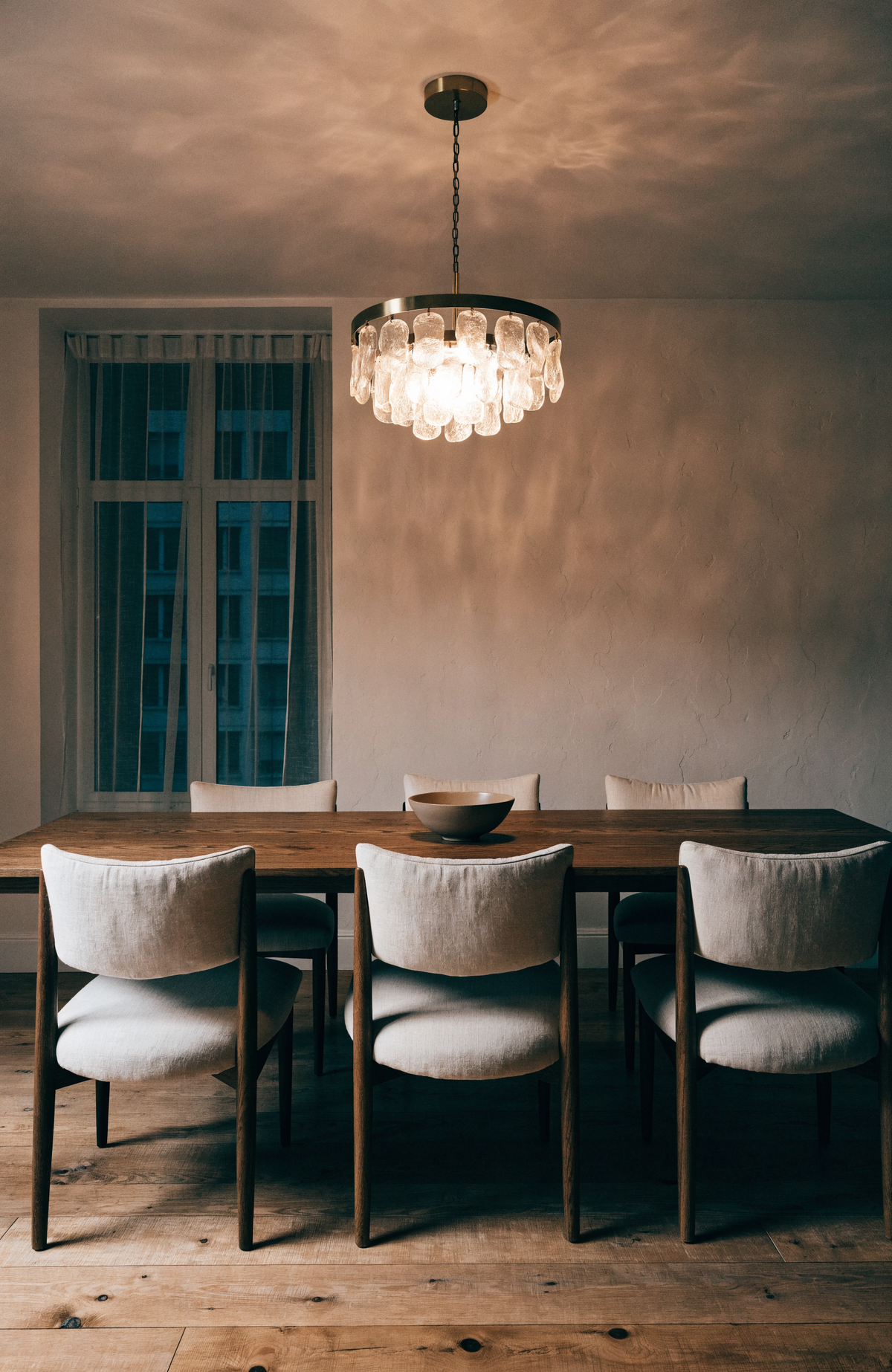 Round brass and glass chandelier centred above a long walnut dining table