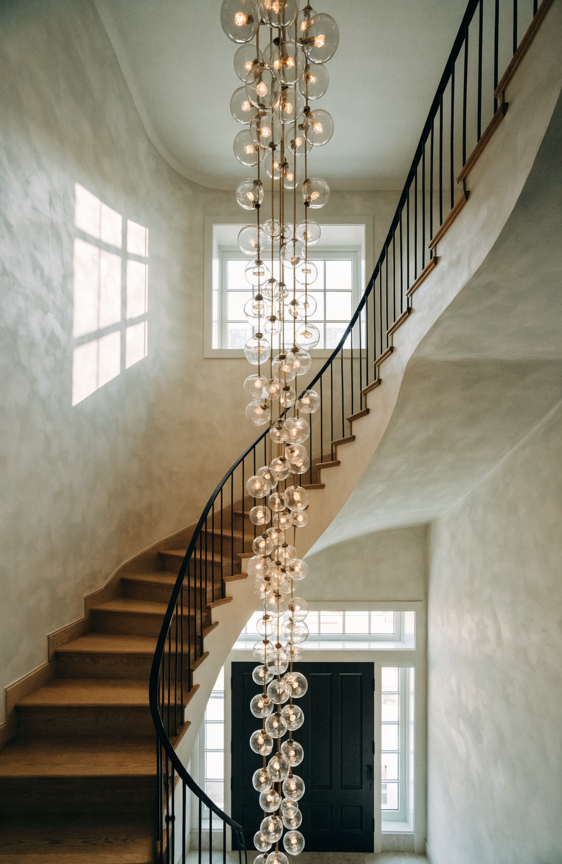 Cascading glass globe chandelier hanging in a double-height entry foyer above a curved staircase