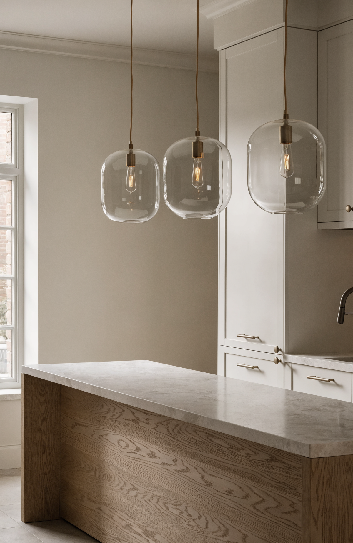Three glass pendant lights hung in a row above a white oak kitchen island