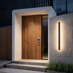 Slim black linear sconce lighting a modern house entrance