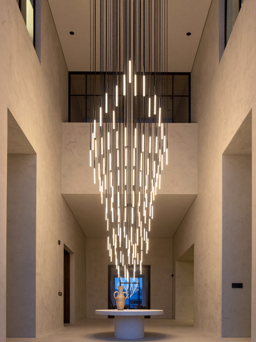 Cylindrical LED staircase chandelier glowing warm white in a double-height entry foyer