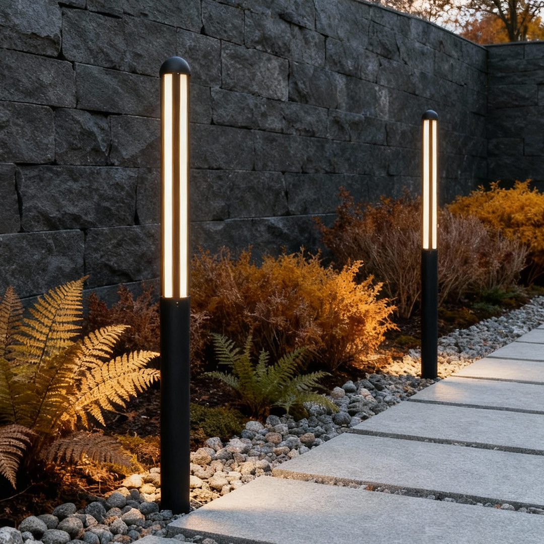 Sleek black bollard light by a stone wall and plants